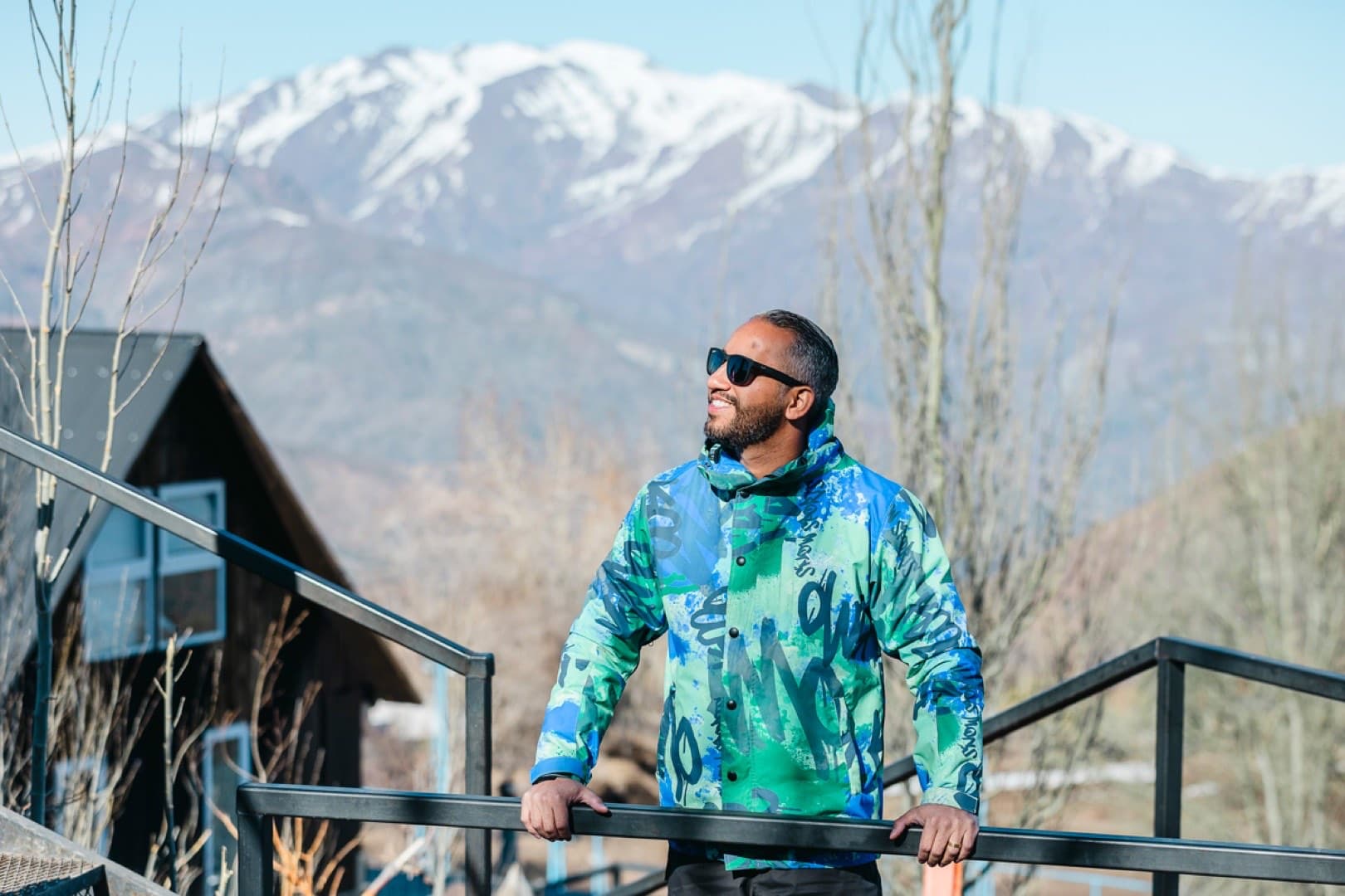 Homem com jaqueta estampada azul e verde com montanhas nevadas ao fundo