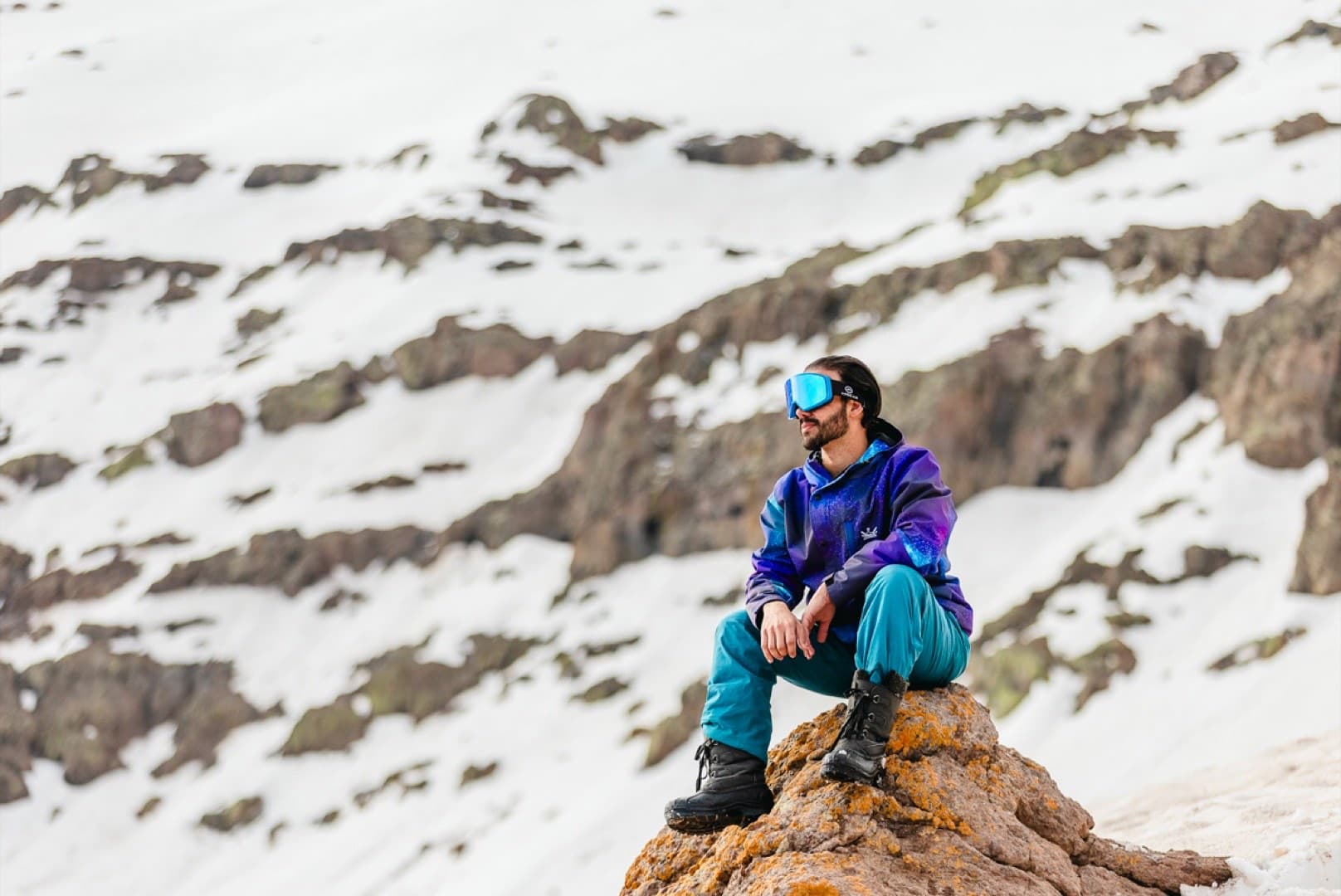 Homem com jaqueta roxa e azul estilosa na montanha nevada